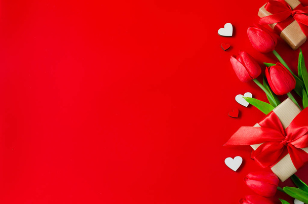 Κόκκινες τουλίπες, κουτιά δώρων και ξύλινες καρδιές σε κόκκινο φόντο. Ευχετήρια κάρτα για την ημέρα του Αγίου Βαλεντίνου. - Φωτογραφία, εικόνα
