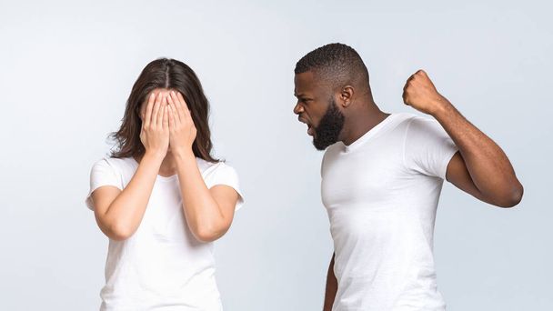 Afro hombre tratando de golpear a su esposa asustada, levantando el puño
 - Foto, Imagen