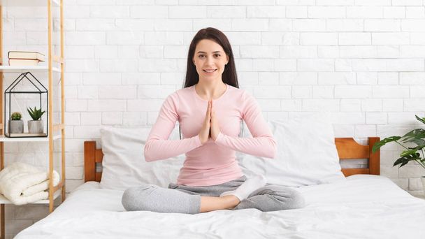 Young woman sitting in lotus position on bed at home - Photo, Image