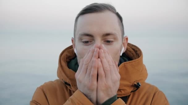 Joven hombre caucásico calentando sus manos en el mar en un día frío
 - Metraje, vídeo