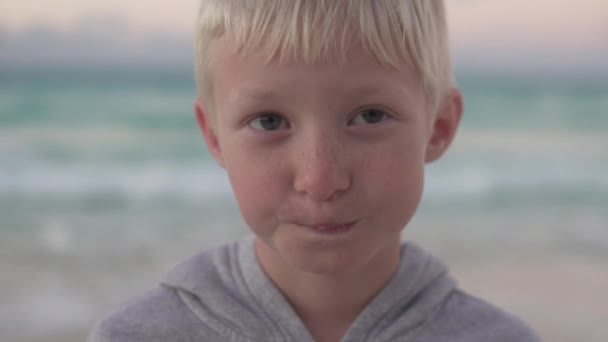 Close-up van een mooie blonde jongen tegen de achtergrond van een uitgespoelde zee - Video