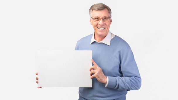 Hombre mayor sonriente sosteniendo afiche en blanco de pie, fondo blanco, panorámica
 - Foto, Imagen