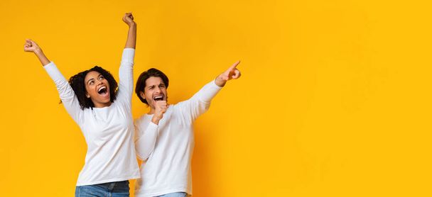 Multiracial couple dancing and singing together, having fun over yellow background - Photo, Image