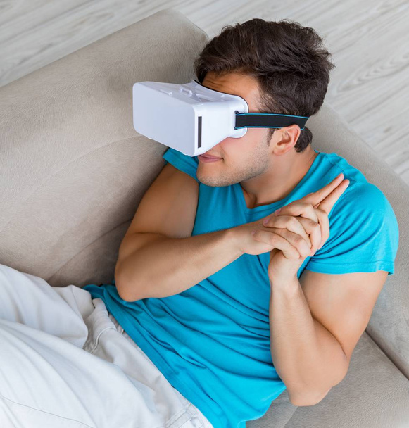 Junger Mann mit VR-Brille entspannt auf Sofa - Foto, Bild
