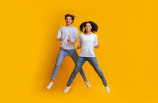 Joyful Interracial Couple Jumping In The Air And Showing Thumbs Up - Foto, immagini