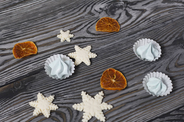 Marshmallows and snowflakes from marshmallows. Nearby dried mandarin slices. On old pine boards painted black. - Zdjęcie, obraz