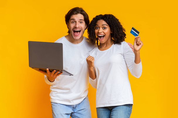 Überglückliches multiethnisches Paar kauft online mit Laptop und Kreditkarte ein - Foto, Bild