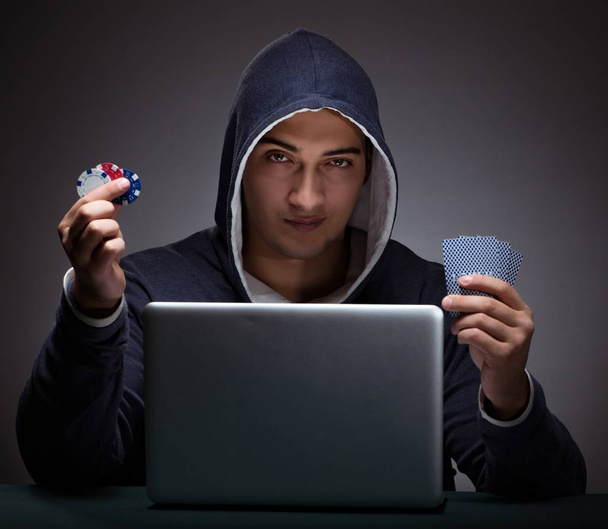 Young man wearing a hoodie sitting in front of a laptop computer - Photo, Image