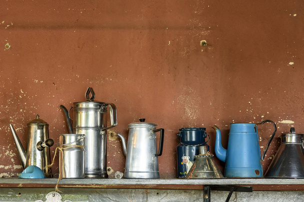 Kolekce starých a použitých hrnců kávy uspořádaných na dřevěné polici s venkovskou stěnou za. - Fotografie, Obrázek