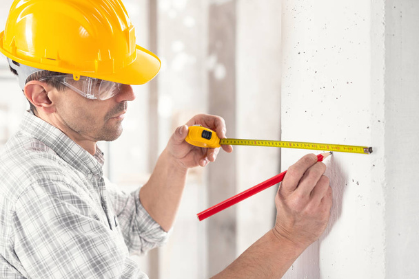 Builder marking measurements on a white wall - Φωτογραφία, εικόνα