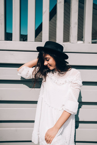 Aurinkoinen elämäntapa muotokuva nuori tyylikäs hipster nainen, yllään trendikäs valkoinen mekko, musta hattu ja saappaat
 - Valokuva, kuva