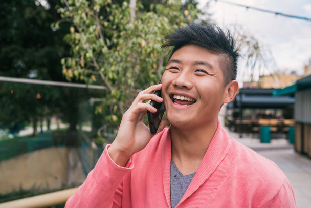 Asian man talking on the phone outdoors. - Фото, изображение