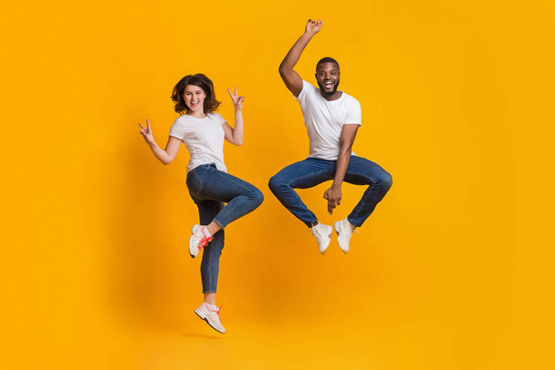 Joyful guy and girl jumping in funny poses on yellow background - Foto, Imagen