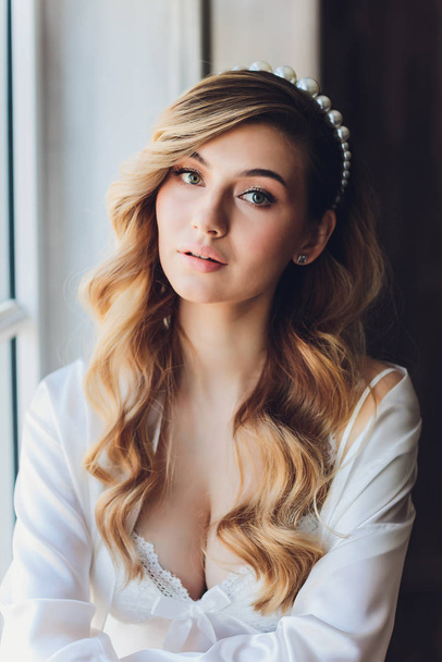 Portrait of a beautiful blonde bride in the interior. Morning young bride in a bathrobe. Wedding photography. Smiling and cute girl stands. - Foto, Imagem