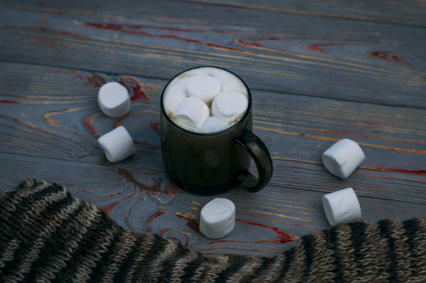 Marshmallow. Retro style wooden background. Glass mug with marshmallow in it. There is also a woolen scarf. Close-up. Tinted - Photo, Image