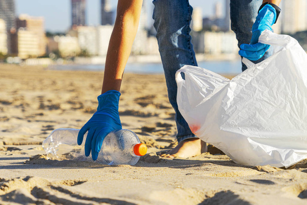 Clean beach from plastic. Hand picking up plastic bottle trash from the beach and putting into plastic bag for recycle - Φωτογραφία, εικόνα