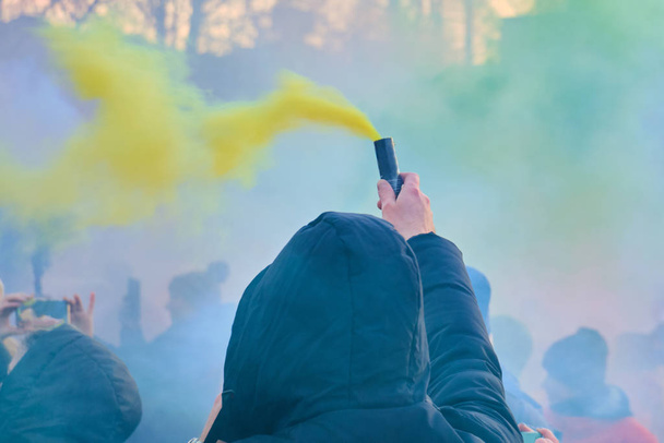 A man in a black hood holds a colored fireworks with a yellow color. - Fotoğraf, Görsel