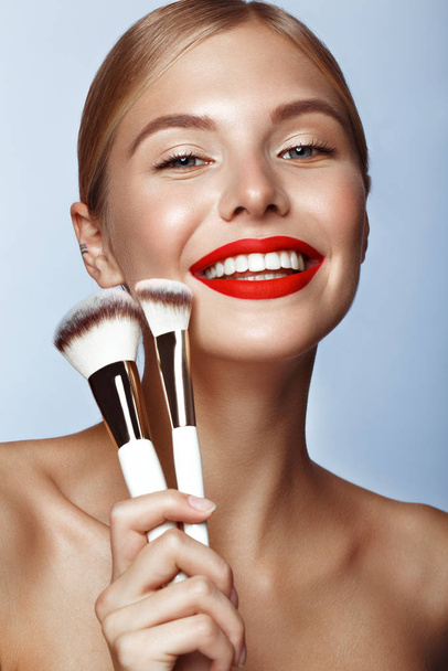 Beautiful girl with red lips and classic makeup with cosmetic brushes in hand. Beauty face. - Foto, Bild