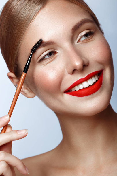 Beautiful girl with red lips and classic makeup with cosmetic brow brush in hand. Beauty face. - Photo, image