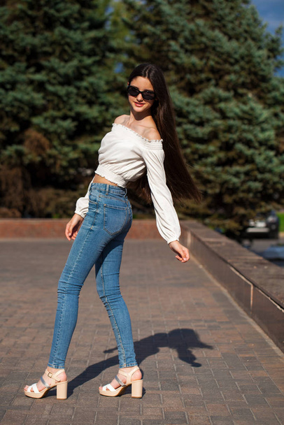 Pretty stylish brunette girl in blue jeans and white blouse  - Valokuva, kuva