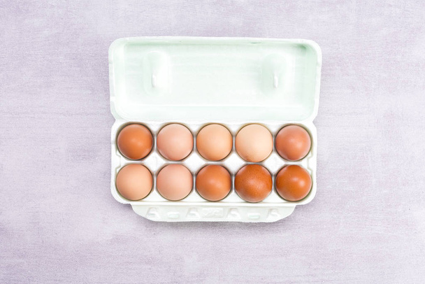 10 brown eggs in a container of white paper on a gray background - Foto, Bild