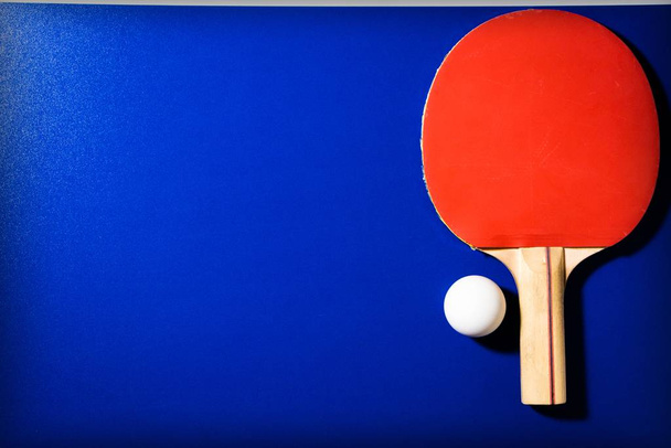 Raqueta roja y pelota para tenis de mesa sobre fondo azul
 - Foto, imagen