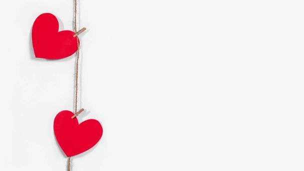 Garland of red hearts on a white isolated banner background. Natural rope and clothespins. The concept of recognition in love, romantic relationships, Valentines Day. Copy space - Фото, изображение