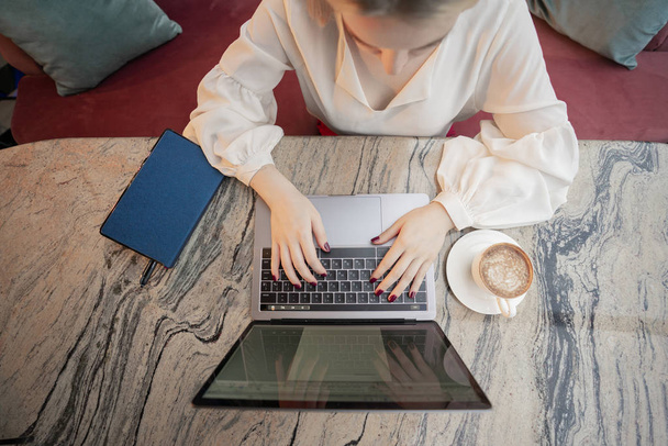 Una joven atractiva mujer de negocios sentada en un café con una computadora portátil y café
 - Foto, imagen