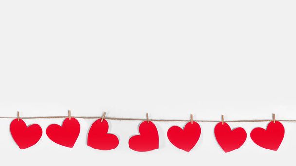 Garland of red hearts on a white isolated banner background. Natural rope and clothespins. The concept of recognition in love, romantic relationships, Valentines Day. Copy space - Foto, Imagen
