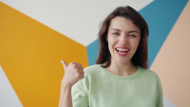 Portrait of happy young lady showing thumbs-up gesture on colorful background - Кадры, видео