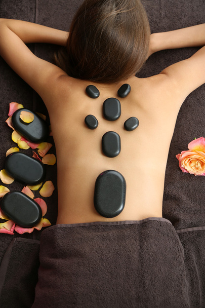 Beautiful young woman having stone massage in spa salon on color background - Foto, Imagen