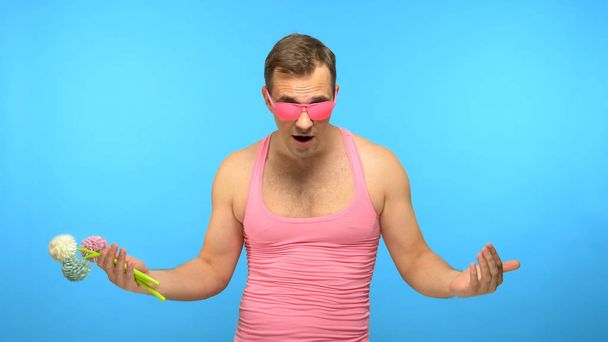 handsome man freak in pink glasses with a bouquet of flowers. blue background - Foto, afbeelding