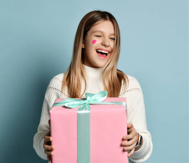 Smiling teen kid girl celebrate valentines day holding a big pink present gifts box for birthday happy laughing on light blue - Foto, Imagem
