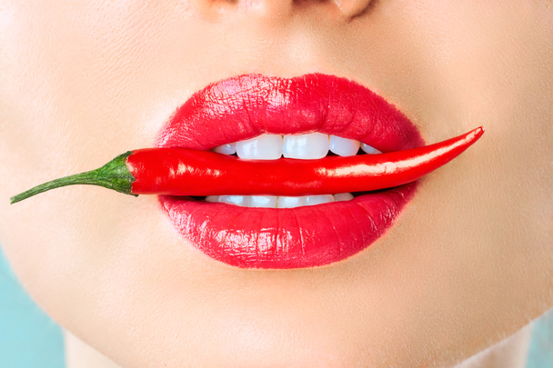 Mujer joven con chile rojo aislado en fondo azul. Sexy labios femeninos. Chica seductora caliente
 - Foto, imagen