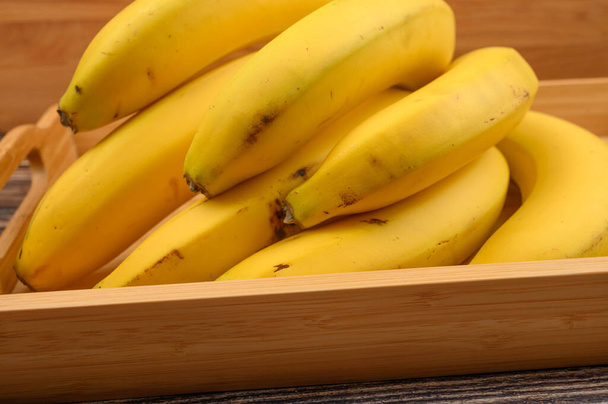 Bunch of ripe yellow bananas on a wooden tray on a wooden background. Close up. - Photo, Image