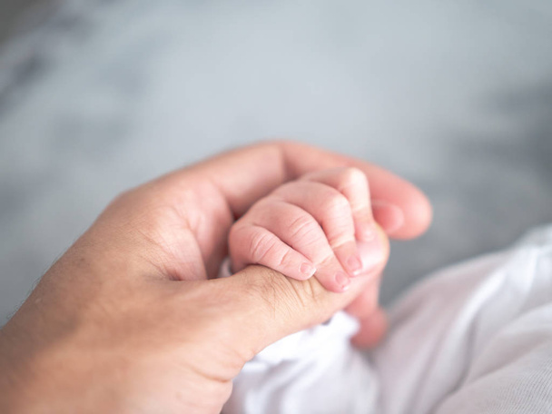A newborn infant boy grabs hold of his dad's thumb as he wraps his tiny fingers around his father's large finger holding on tight. - Foto, Bild