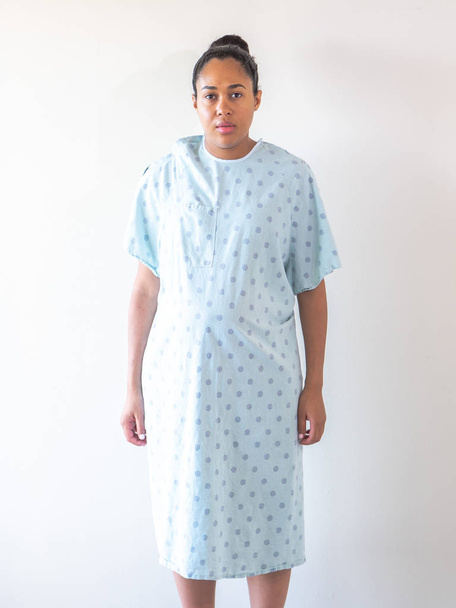 Un post-partum de mère portant une robe d'hôpital ou une robe se tient face à la caméra en regardant à blanc
. - Photo, image