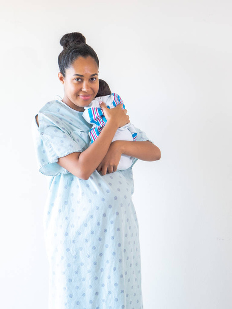 Een gemengd ras Afro-Amerikaanse moeder draagt een ziekenhuis toga houdt haar gloednieuwe baby op haar schouder knuffelen en wiegen hem als hij slaapt in zijn deken swaddle. - Foto, afbeelding