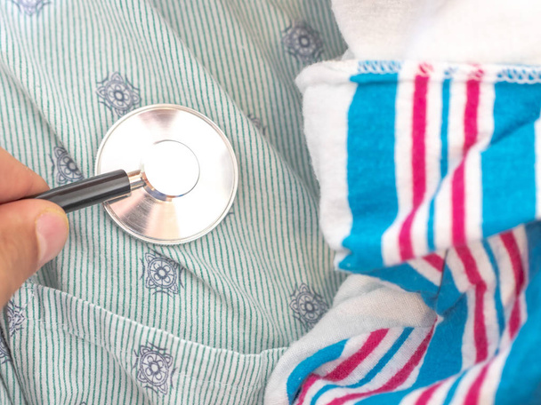 A closeup of a doctor holding a stethoscope to a mixed race African American woman's chest as she holds her swaddled newborn infant baby against her hospital gown making a great medical background. - Photo, Image