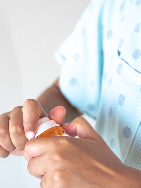 Uma jovem de raça mista afro-americana vestindo um vestido de hospital azul estampado ou roupão desaperta a tampa de um recipiente de medicação ou pílula de plástico para consumir
. - Foto, Imagem