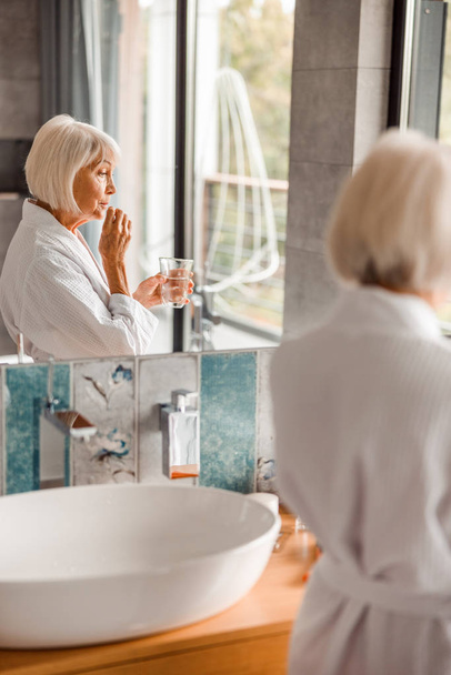 Senior lady in bathrobe taking pills in bathroom - Фото, зображення
