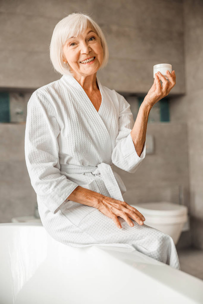Cheerful elderly woman holding jar of cream - Valokuva, kuva