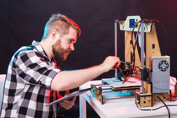 Technologia i koncepcja inżynieryjna - Mężczyzna inżynier pracujący w nocy w laboratorium, dostosowuje komponenty drukarki 3D. - Zdjęcie, obraz