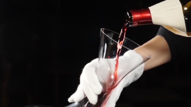 Pincészet koncepció. Vörösbor öntött bor dekanter sötét háttérrel. Közelkép a vörösboros üveg nyakáról, ami a kancsóba ömlik. Lassított felvétel. Borleépülés. Teljes hd - Felvétel, videó
