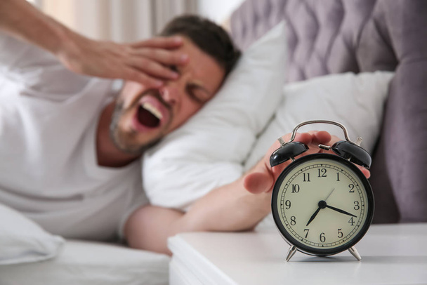 Sleepy man turning off alarm clock at home in morning, focus on  - Foto, Bild