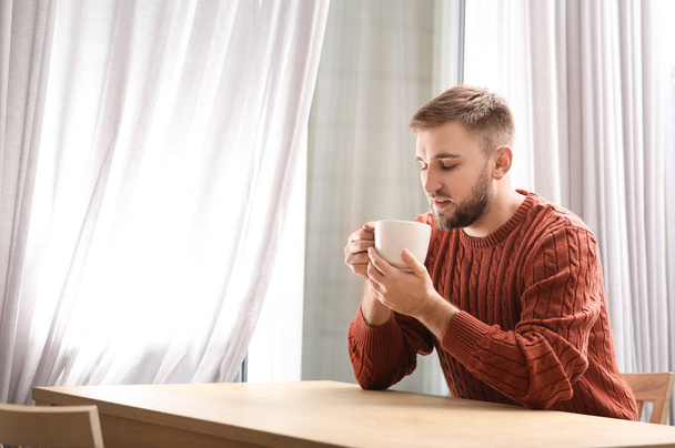 Young man with cup of hot drink near window at cafe - Foto, Bild