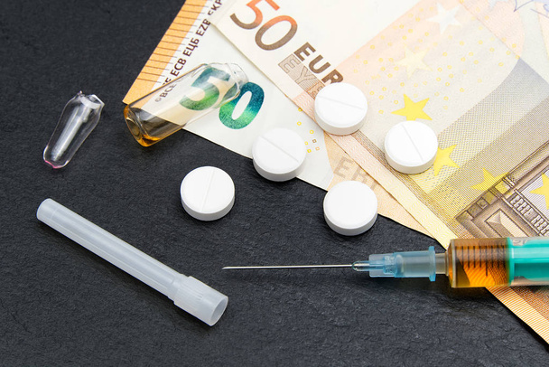 Soldi e pillole con farmaci e una siringa su nero
 - Foto, immagini
