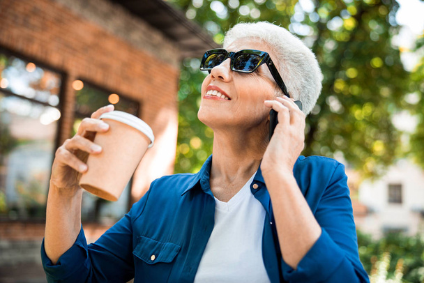 Joyful senior woman having phone conversation outdoors - Foto, Imagen