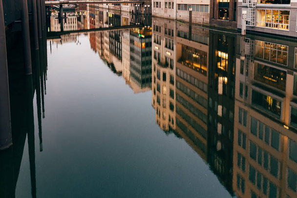 Vista panorâmica dos reflexos de edifícios e luzes sobre a água no canal Bleichenfleet em Hamburgo
 - Foto, Imagem