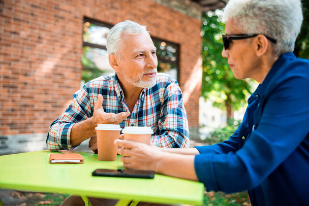 Smiling elderly man talking with lady in outdoor cafe - Foto, Imagen